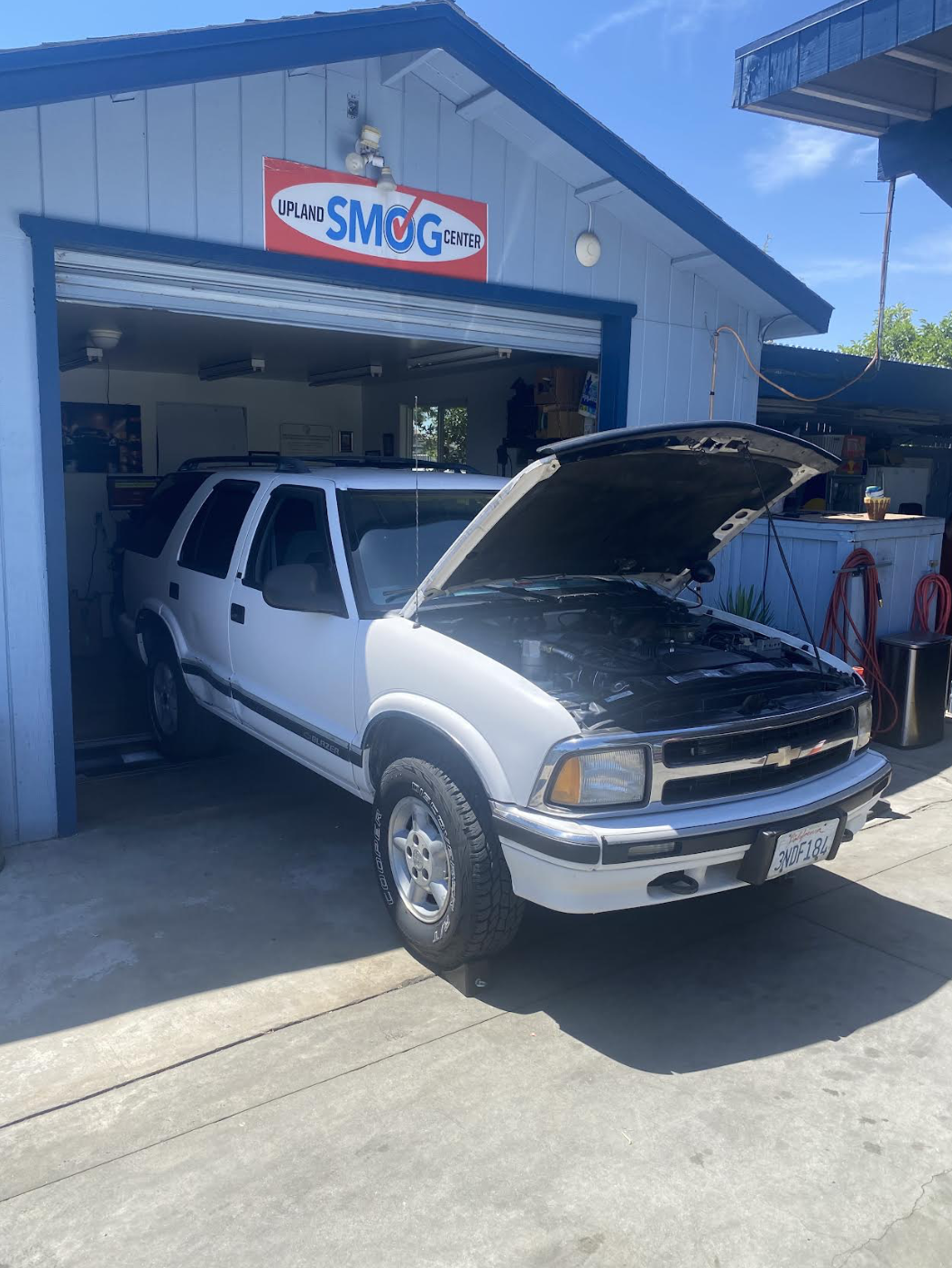 White Chevrolet Blazer with hood open inside the Upland Smog Center garage bay