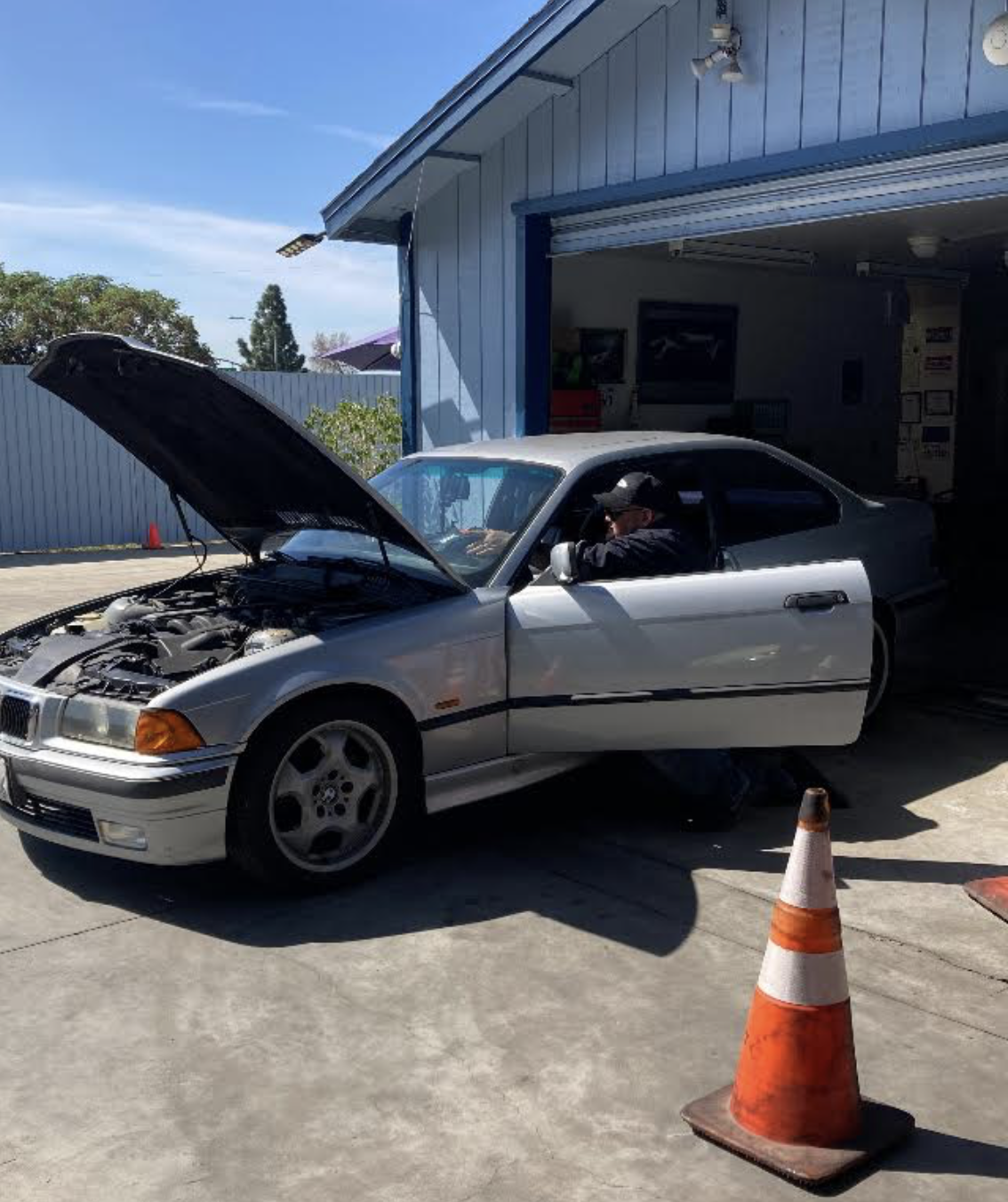 Silver BMW coupe parked outside the blue garage with its hood open